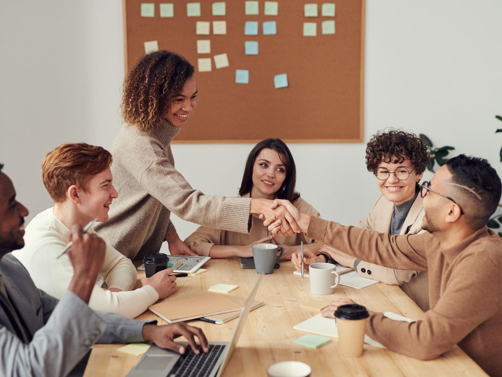 A diverse group of professionals collaborating around a table in a bright, modern workplace — introductions and a warm handshake between colleagues.