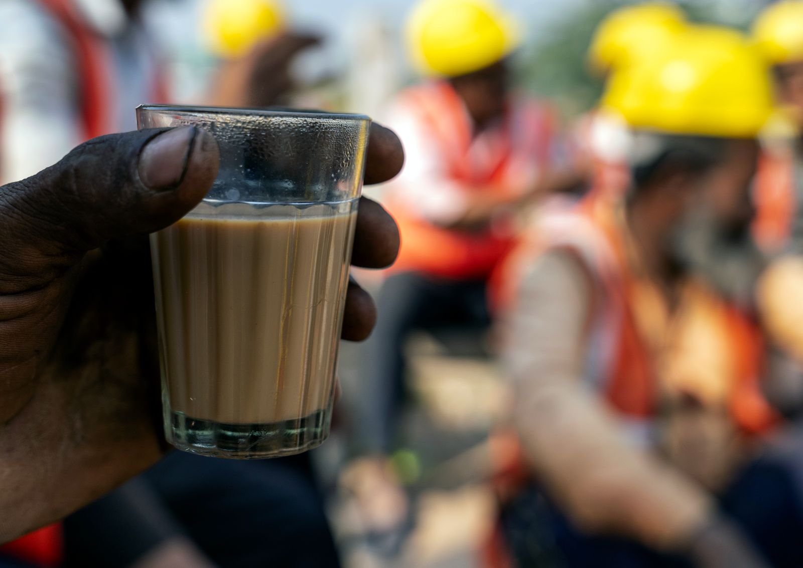 A construction crew taking a quiet break together outdoors, one worker holding a cup in the foreground.