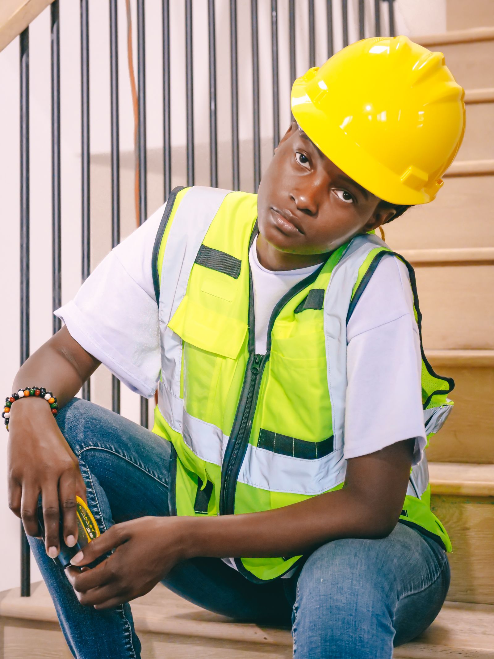 A young trades worker in a hard hat and safety vest sitting quietly on a job-site staircase.