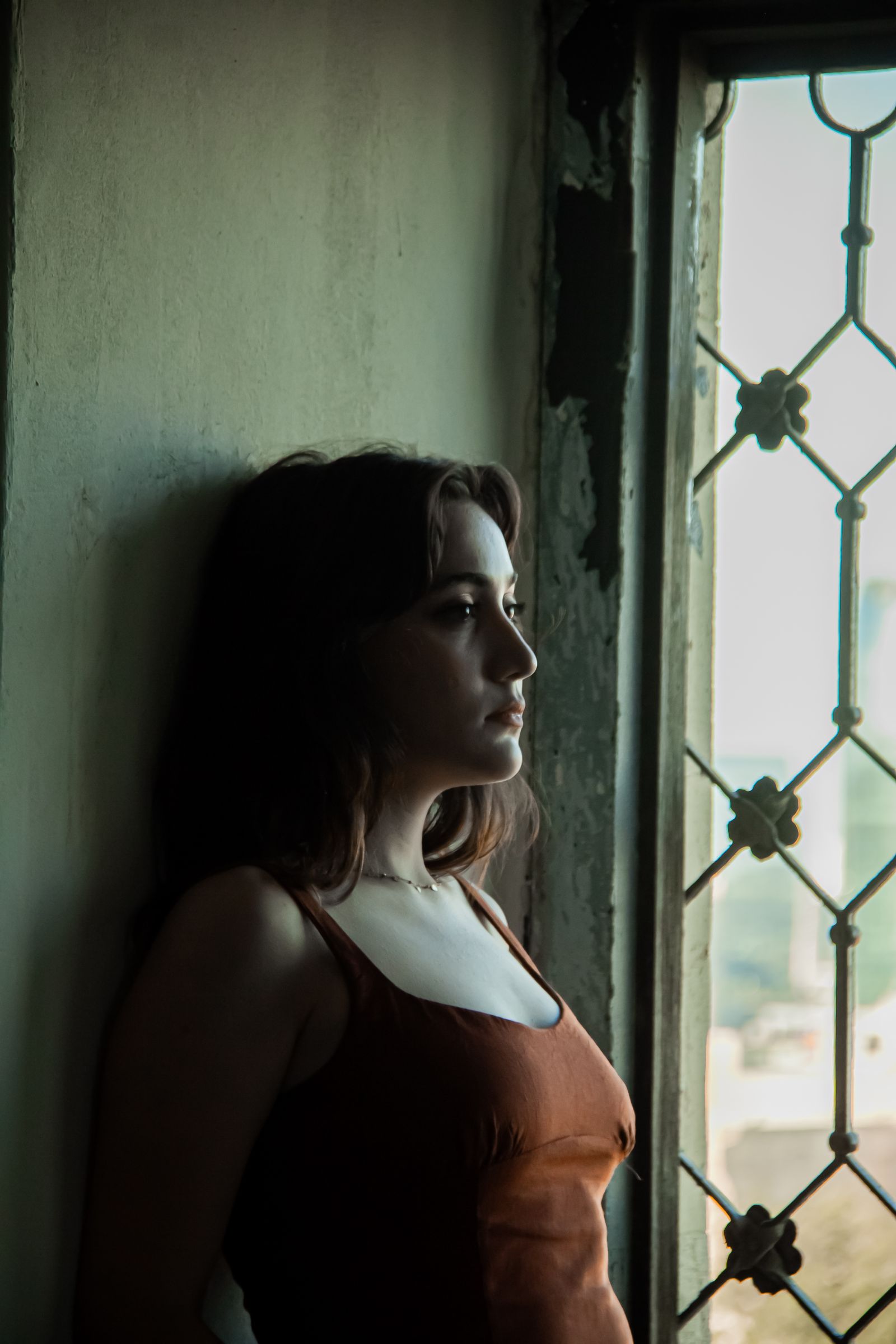 Adult standing quietly by a window in soft natural light, thoughtful expression.