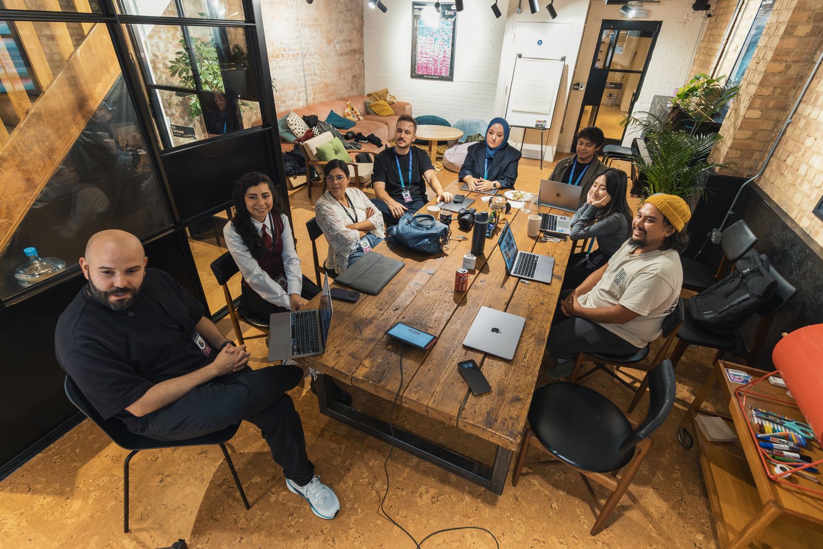 A diverse team gathered around a wooden meeting table in a bright industrial space.