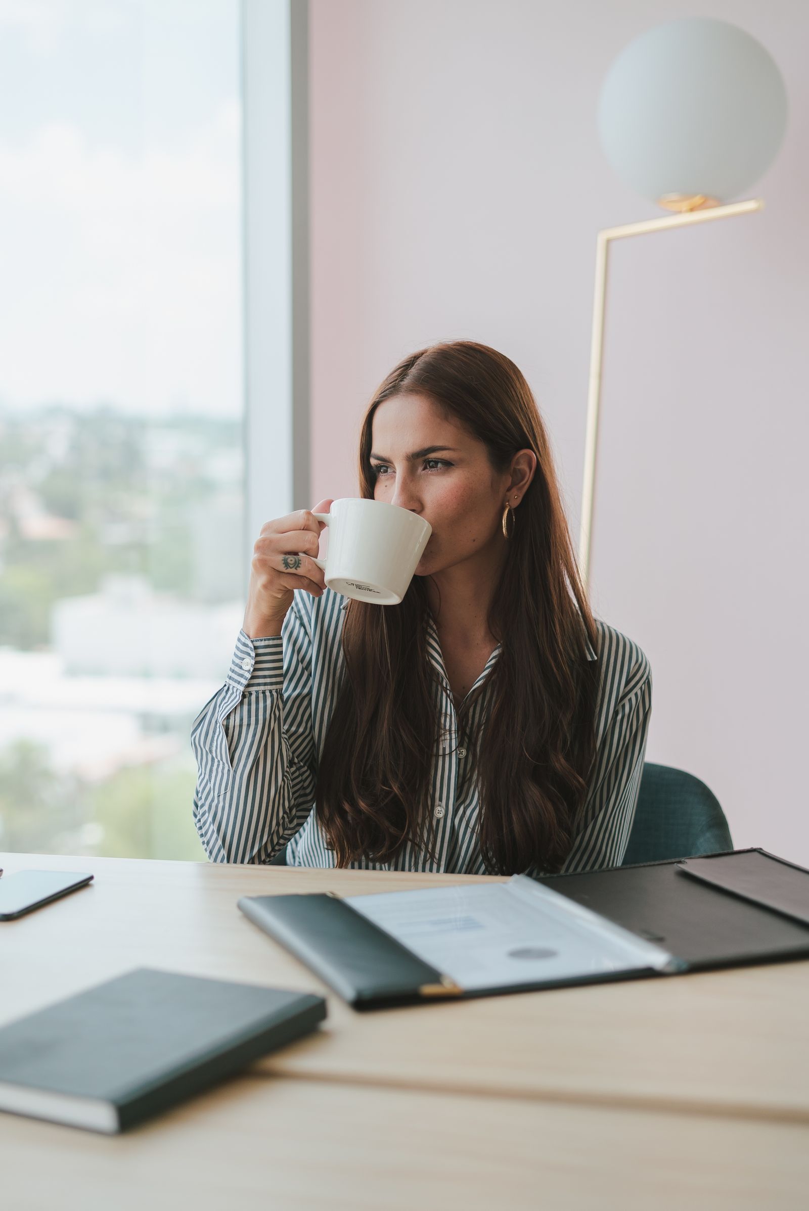 A young professional pausing for coffee at an office desk with paperwork nearby.