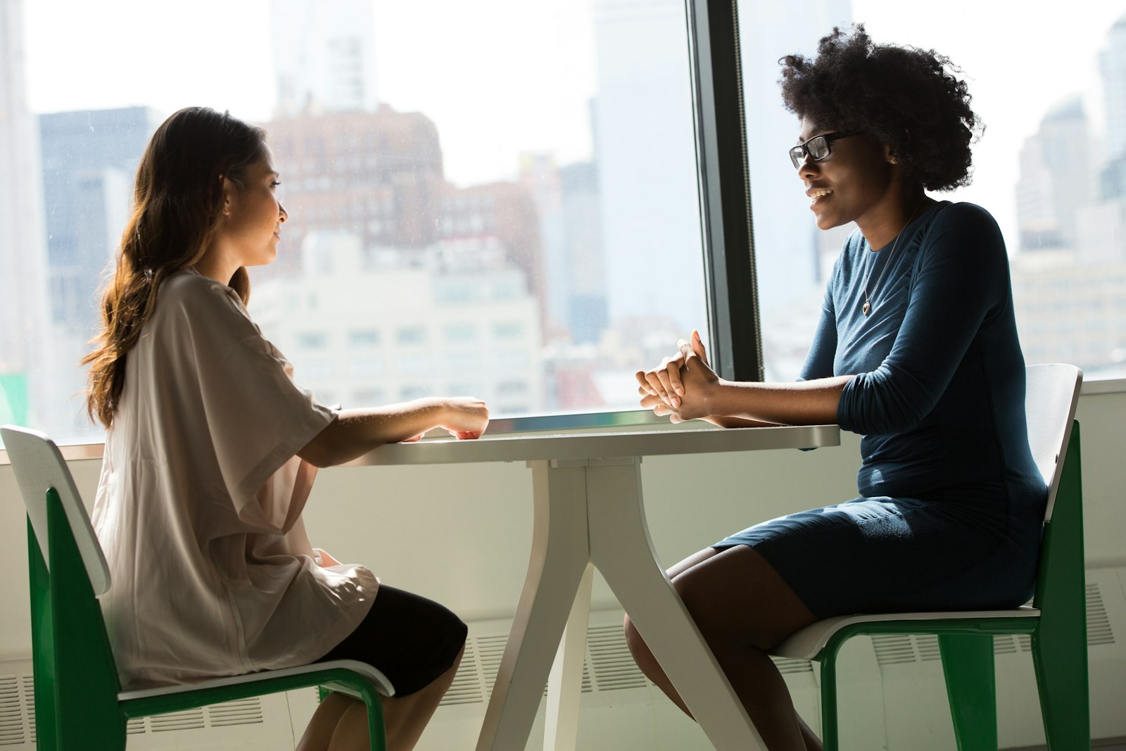 Two professionals seated at a small table by a window in a calm, supportive one-on-one conversation.