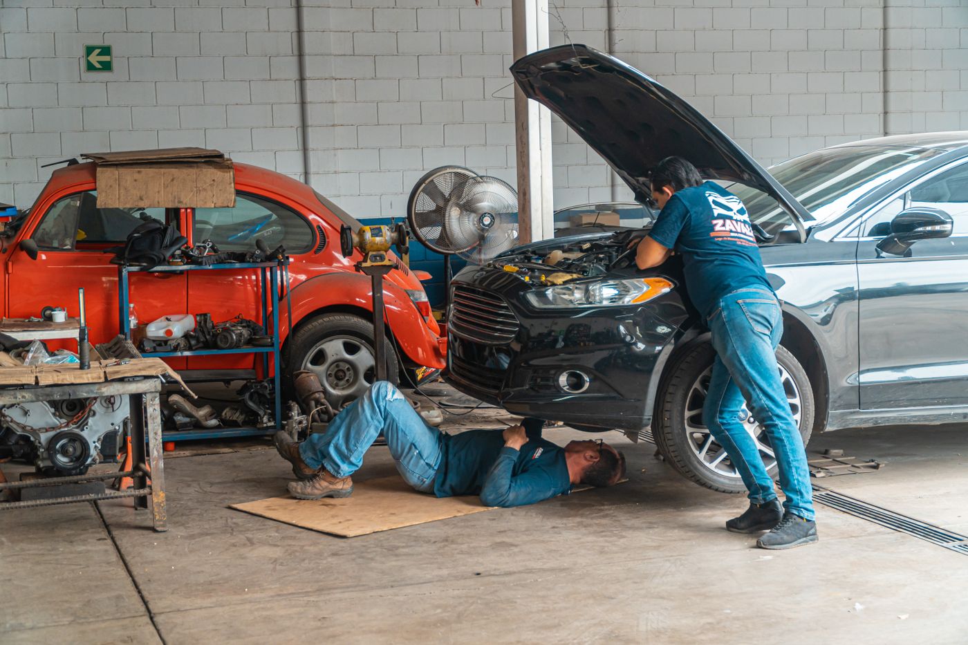 Two automotive service technicians working together on a vehicle inside a dealership service shop.