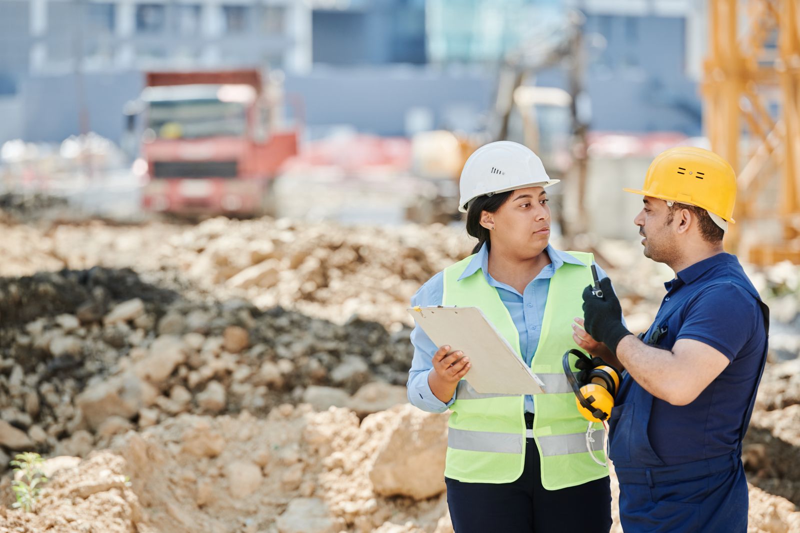 Two construction workers in hard hats and safety vests having a natural conversation on an active jobsite.