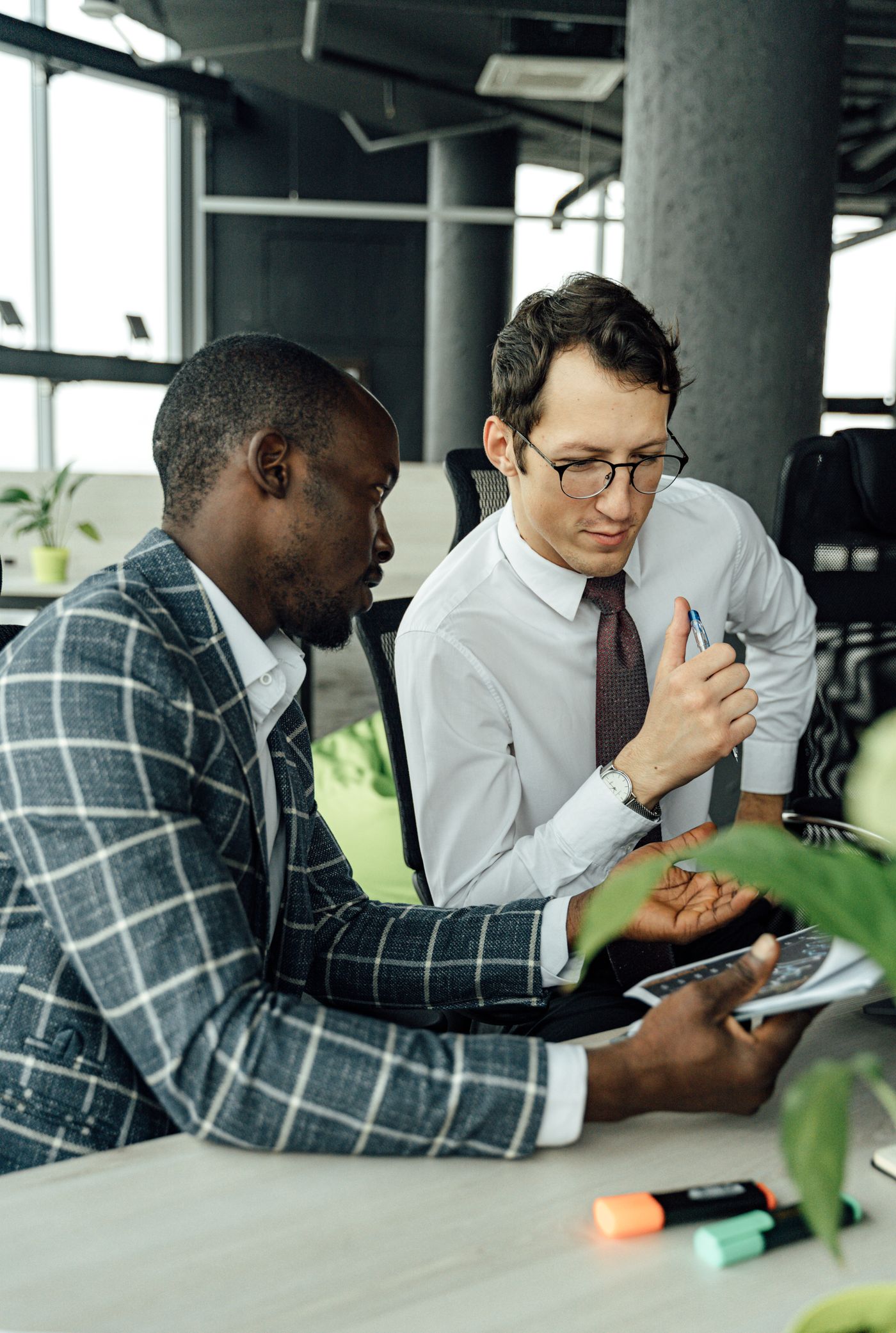 A supportive workplace conversation between two colleagues in an open office, one leaning in to listen.
