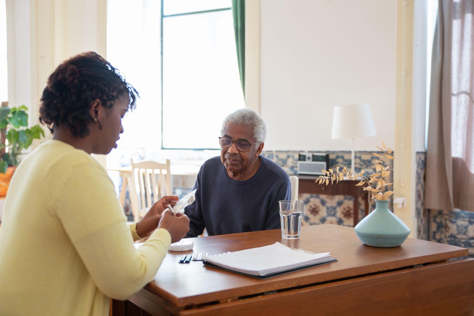 A caregiver in a warm, unhurried conversation with an older adult resident at a home dining table.