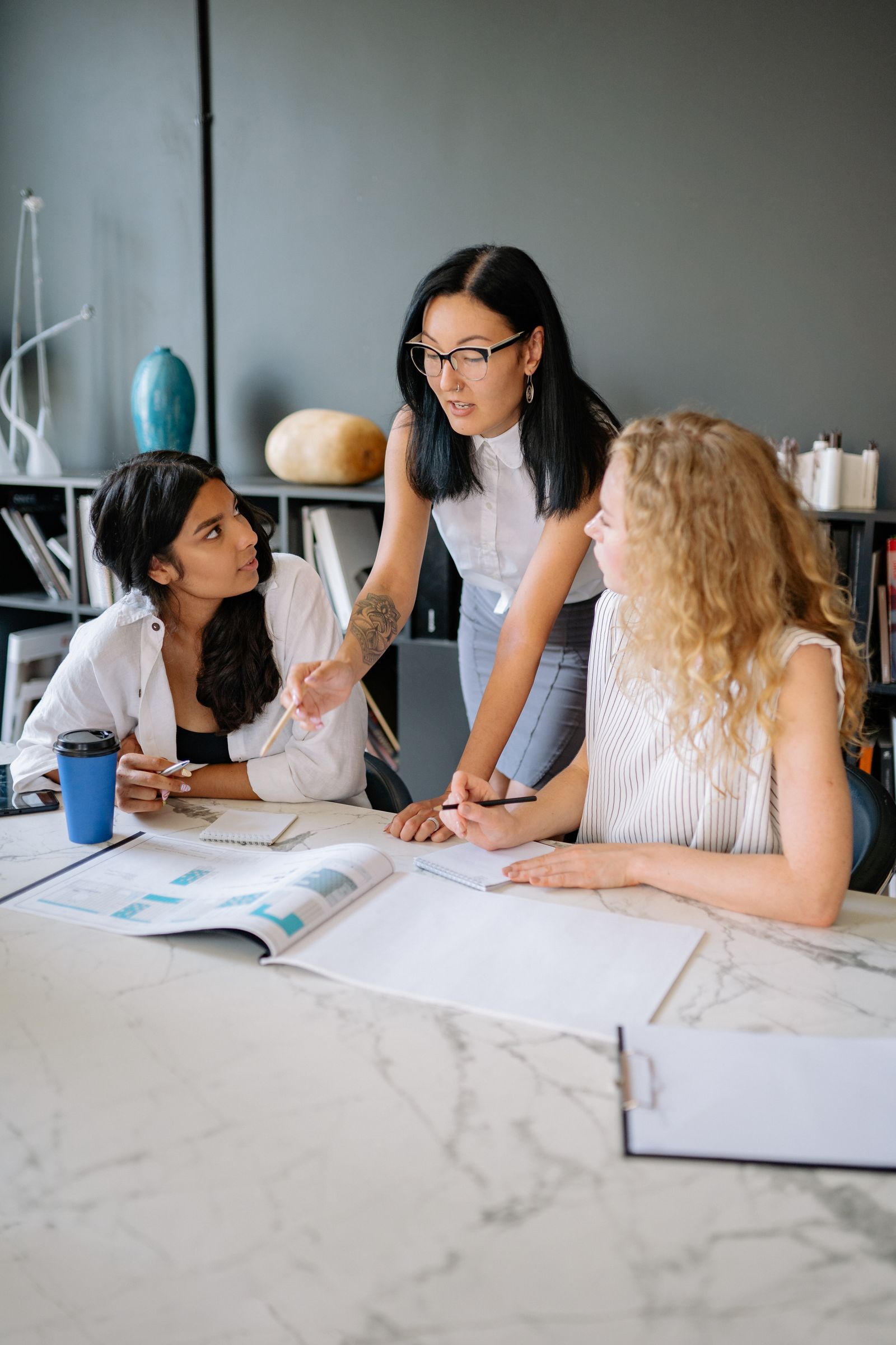 A facilitator standing at a workplace table, guiding a small group of employees through an engaged, practical discussion.