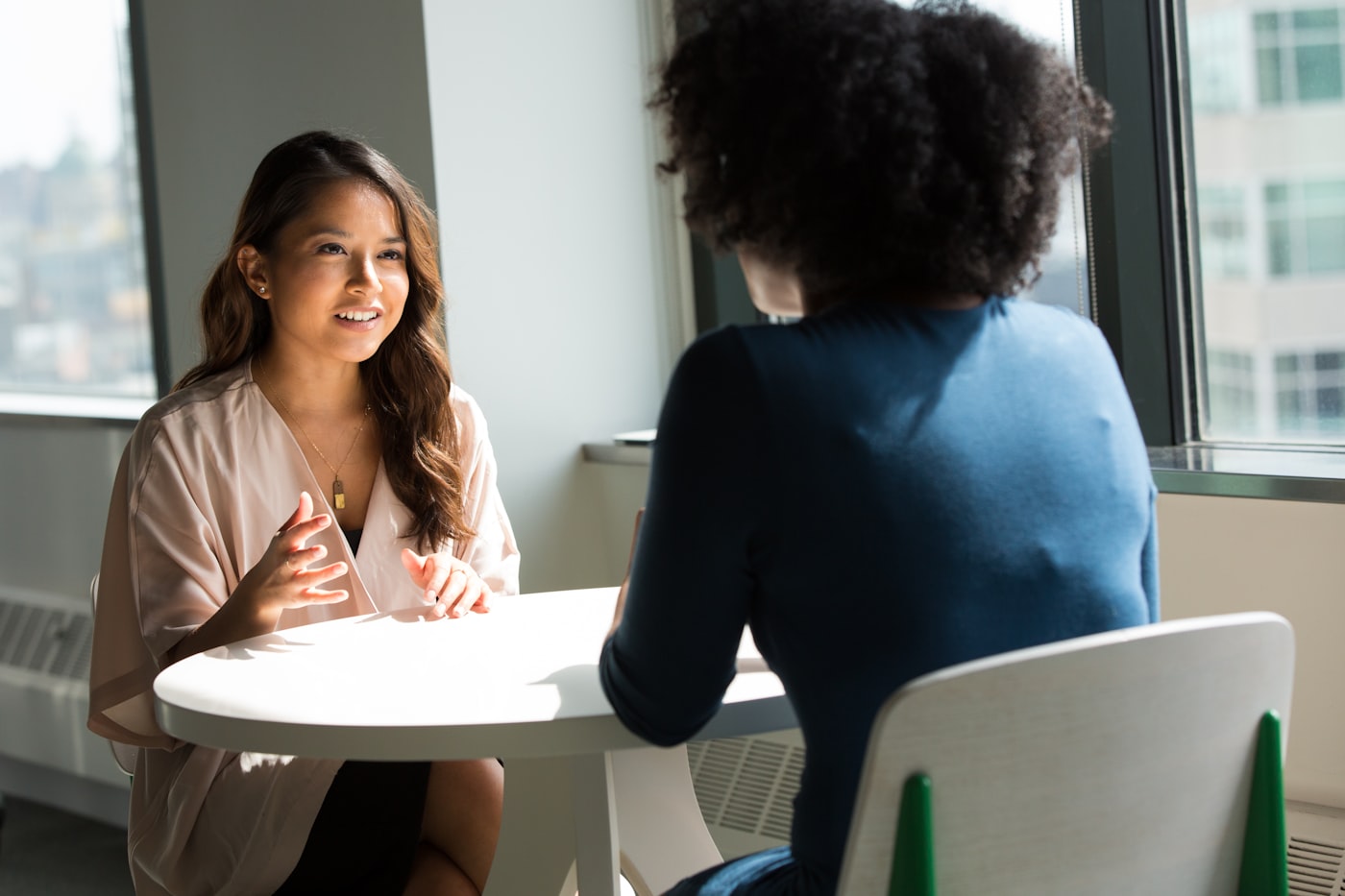 Two coworkers sitting at a small office table in a quiet, supportive one-on-one conversation.